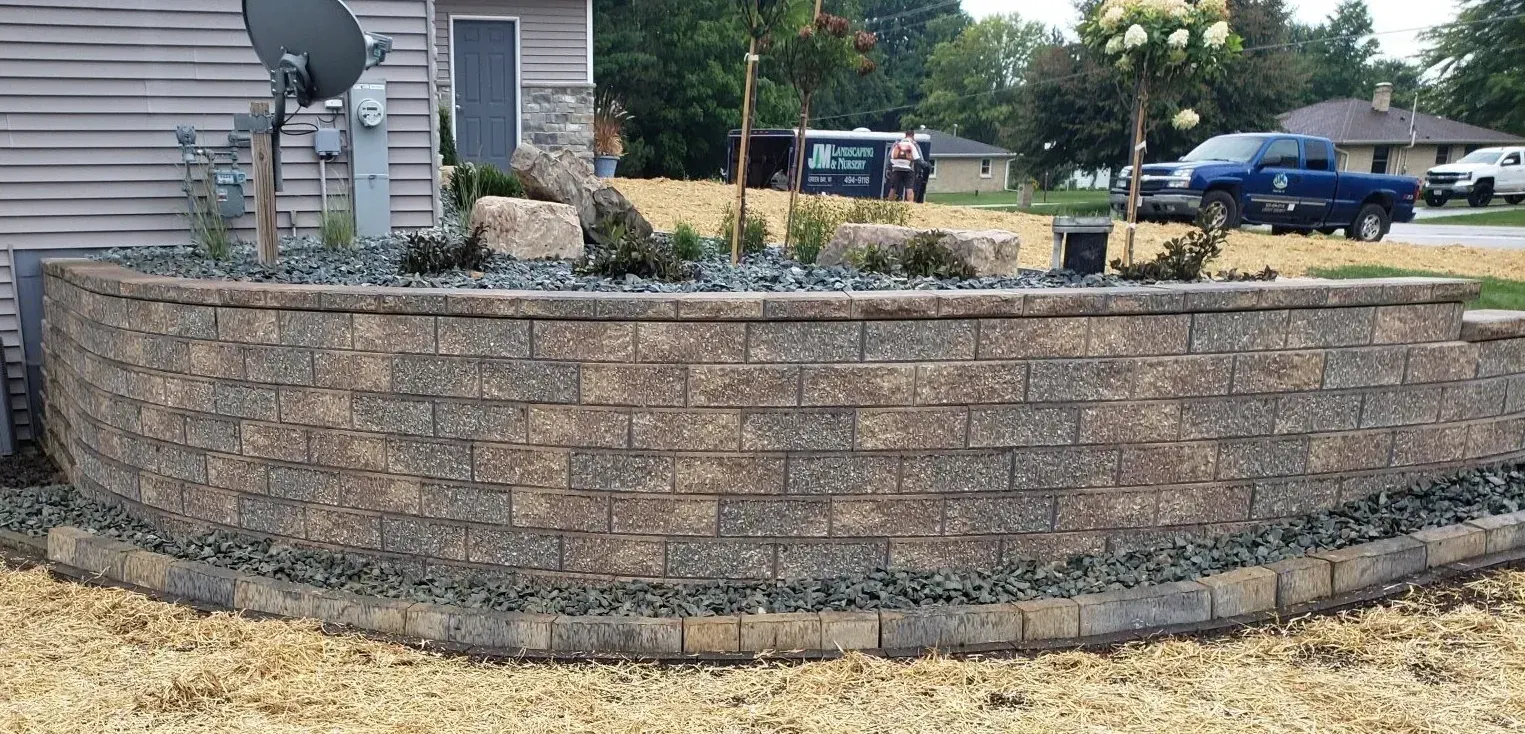 Tall block retaining wall holding a raised planting bed with a newly planted tree