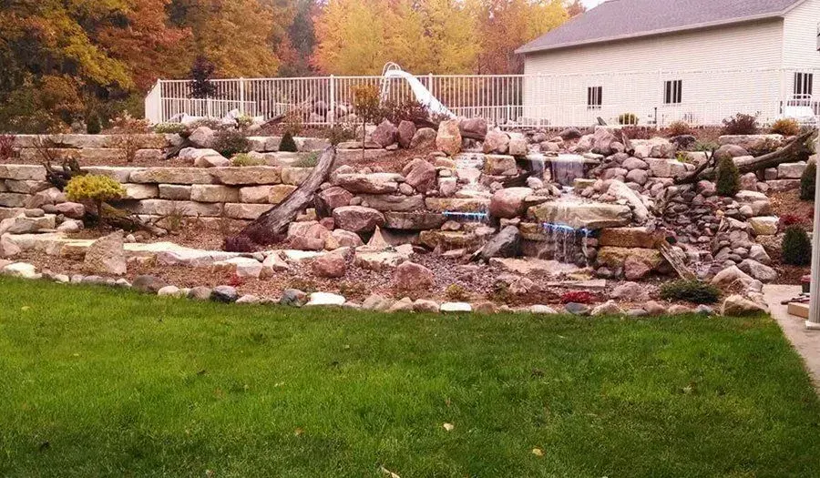 Large boulder waterfall spilling into a backyard pond among autumn trees