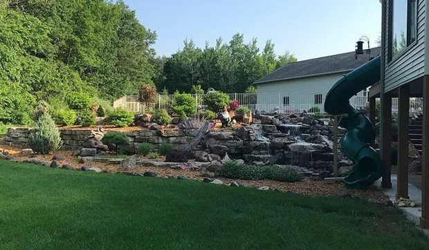 Boulder waterfall and rock garden stepping down to a backyard lawn