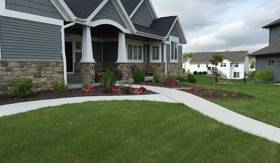 Craftsman home entry with red annuals, low shrubs and a concrete walkway
