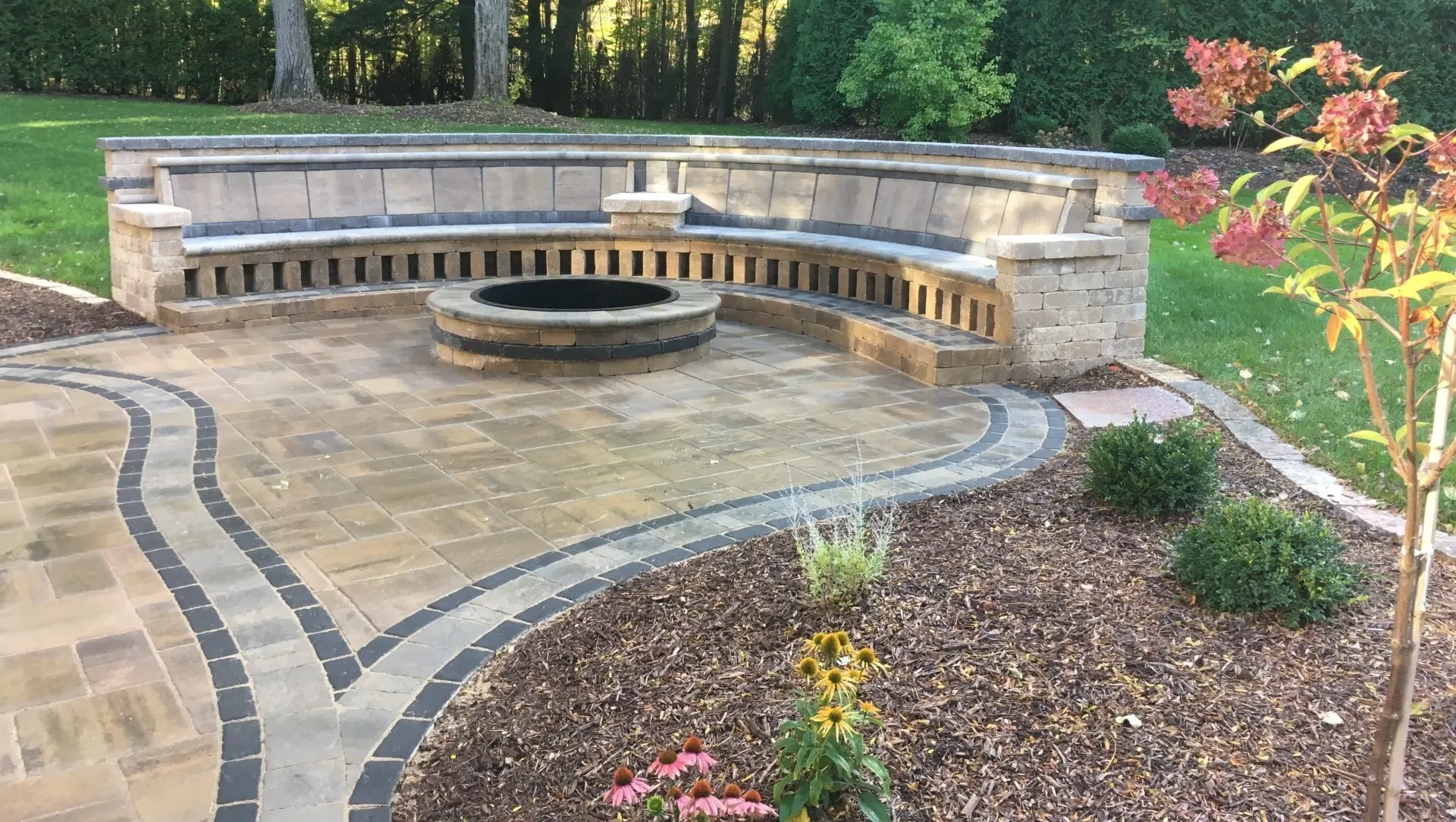 Sweeping paver patio with a built-in fire pit and curved stone seat wall