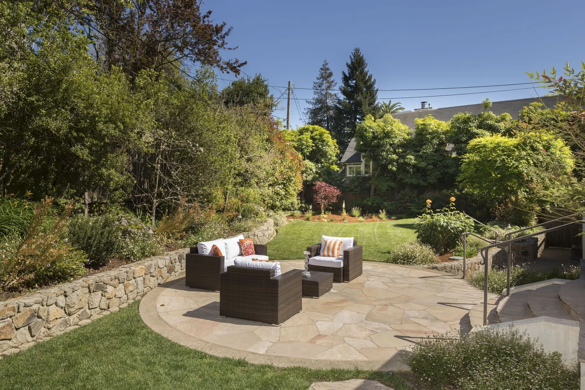 Round flagstone patio with cushioned wicker chairs beside a planted stone wall