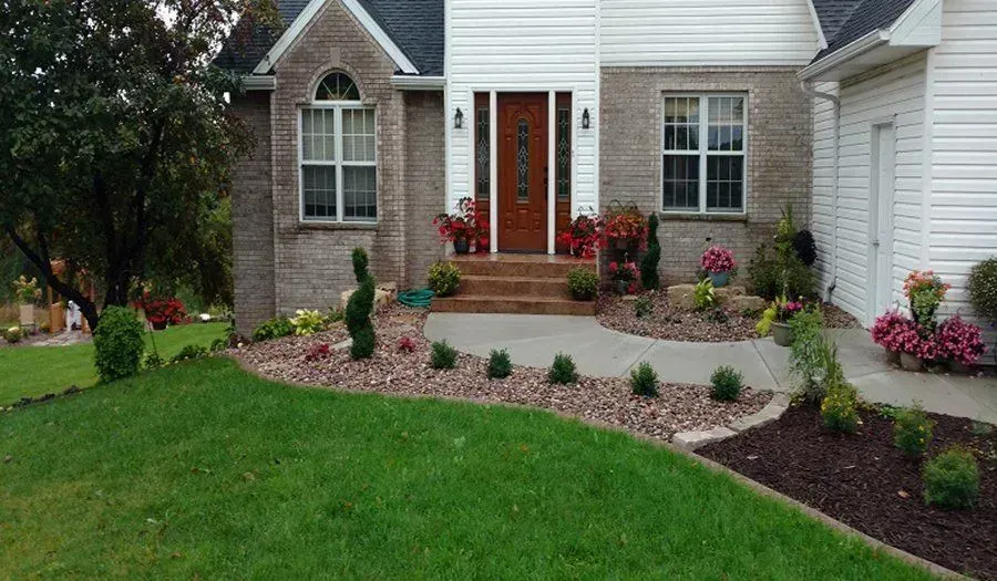 Front entry landscaping with red flowering shrubs along a curved sidewalk