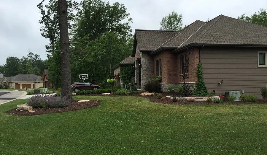 Shrub beds and accent boulders framing the front lawn of a stone-and-brick home
