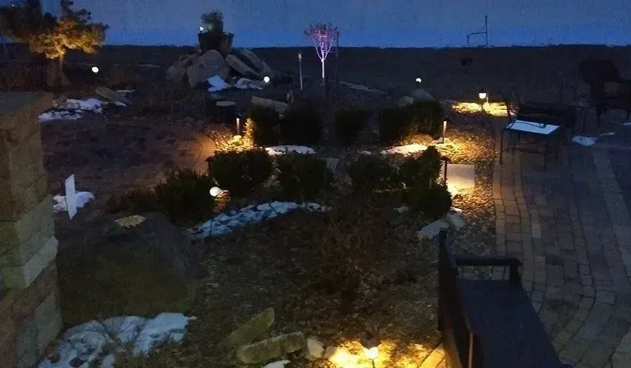 Landscape lights highlighting evergreen shrubs and boulders on a winter evening