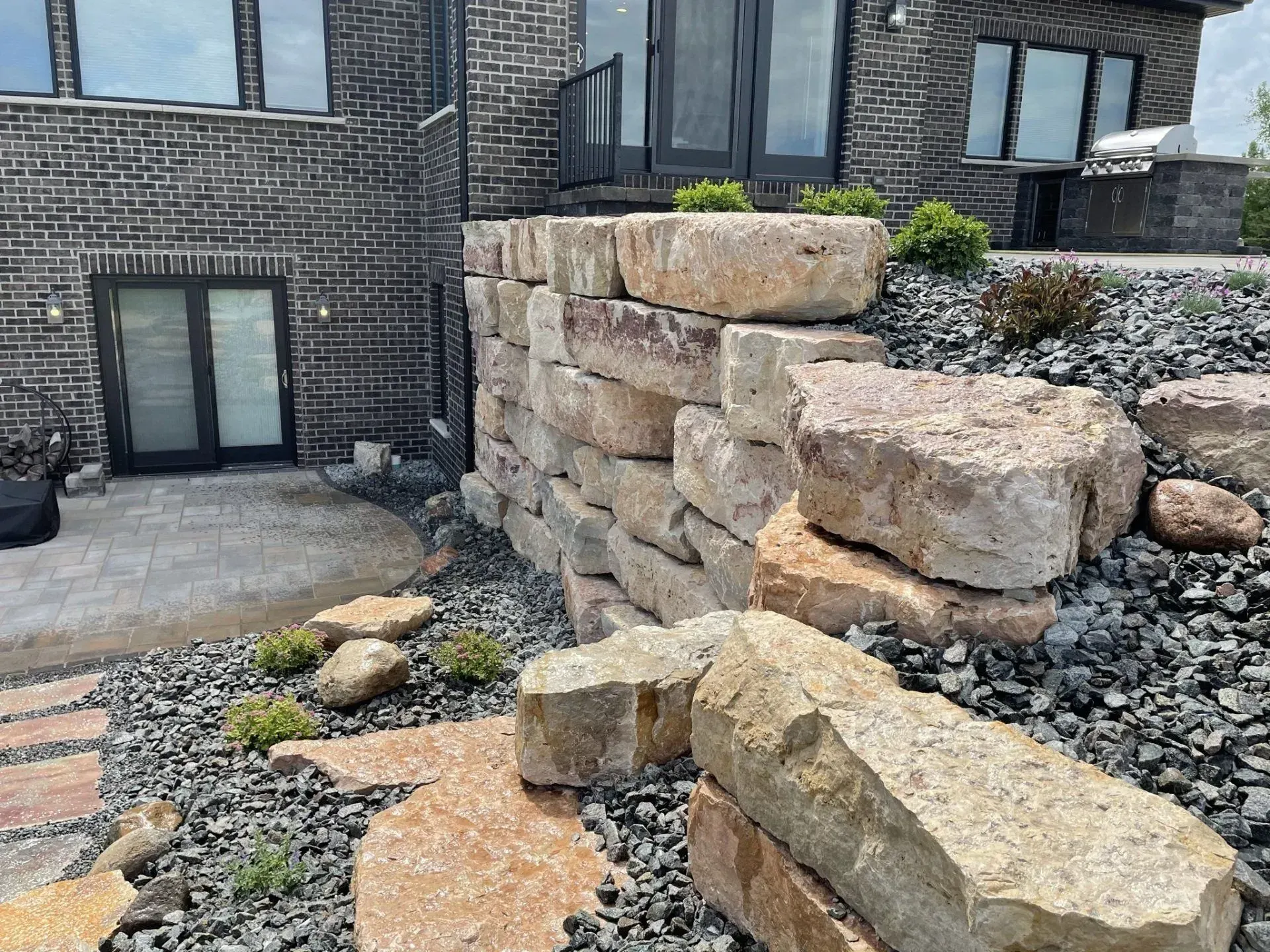 Limestone boulder wall and river rock bed against a modern brick home