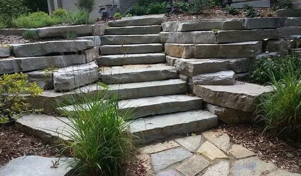 Stone slab stairway set between stacked boulder walls and ornamental grasses