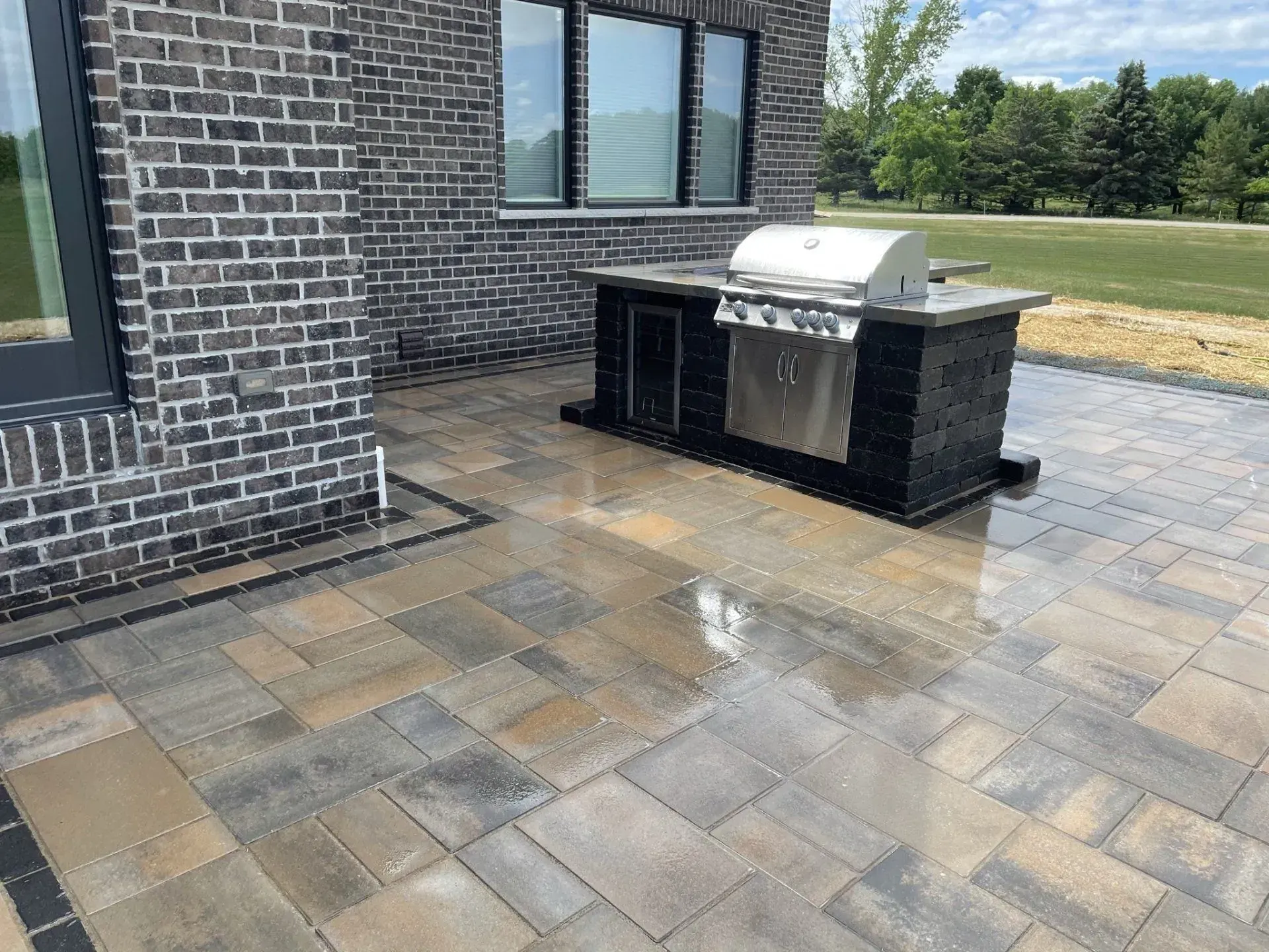 Outdoor kitchen island with a stainless grill on a rain-washed paver patio