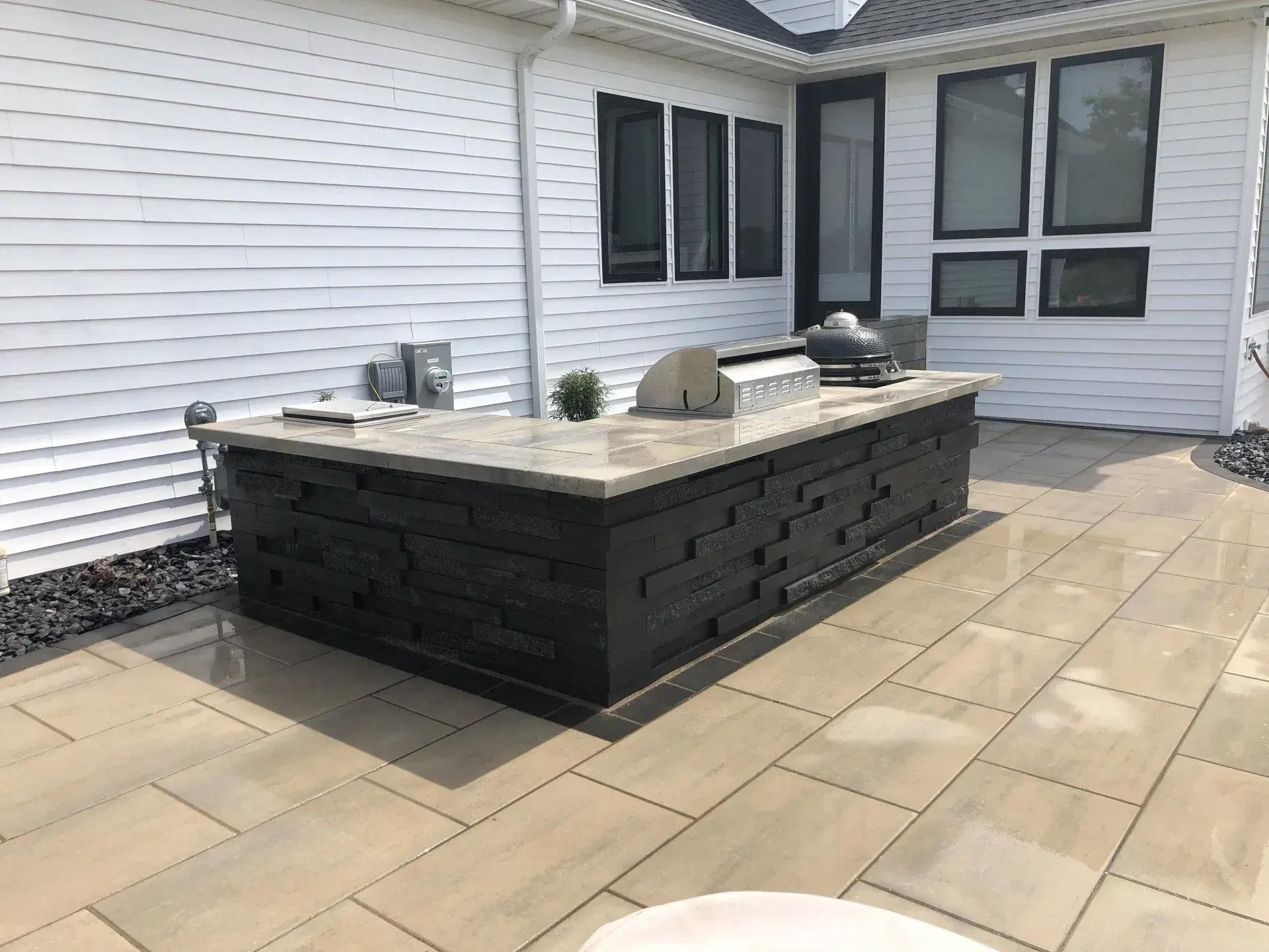 Outdoor kitchen island with a stainless grill on a paver patio at a white home