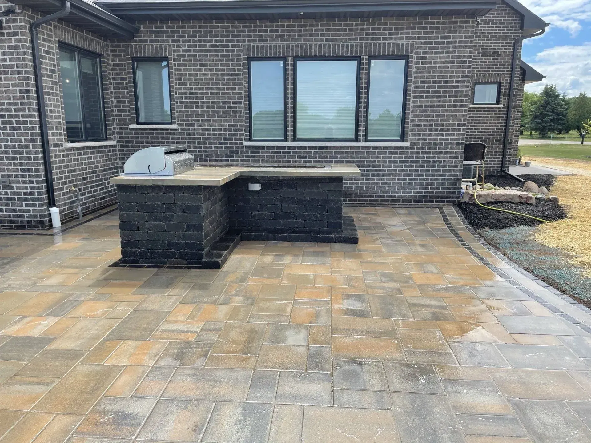Built-in grill island anchoring a large paver patio at a brick home