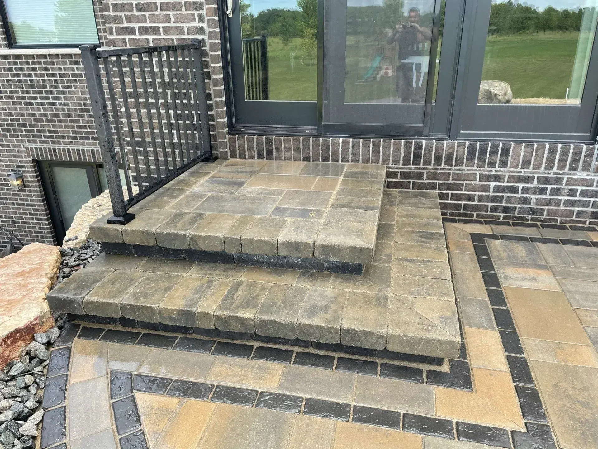 Paver entry steps with a black metal railing at a brick home's patio door