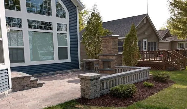 Paver patio with stone seat walls and an outdoor fireplace beside a blue home