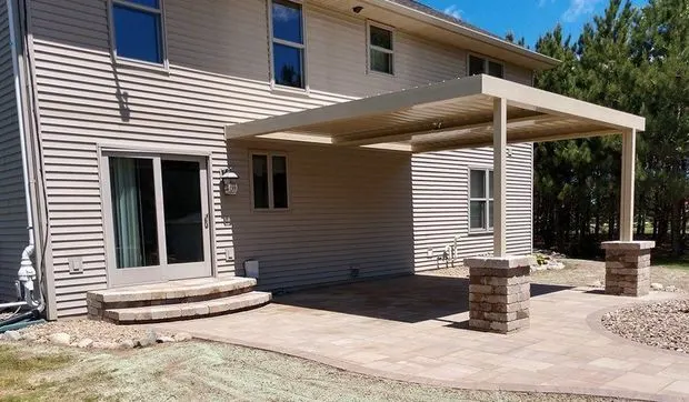 Large paver patio sheltered by a pergola on stone columns