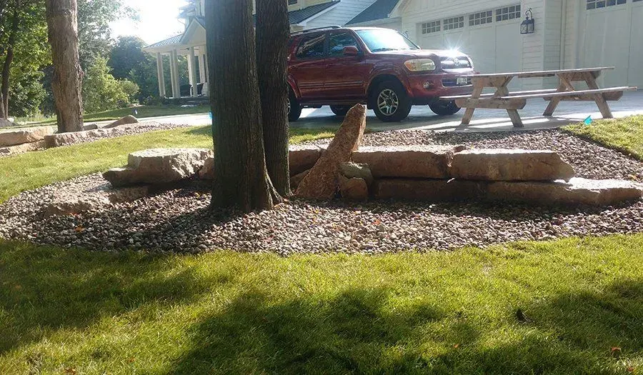 Mulched planting ring around a shade tree backed by a low boulder wall