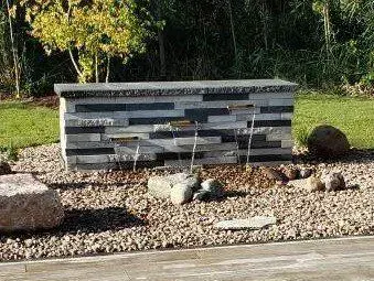 Modern stacked stone wall water feature spilling into a river rock basin